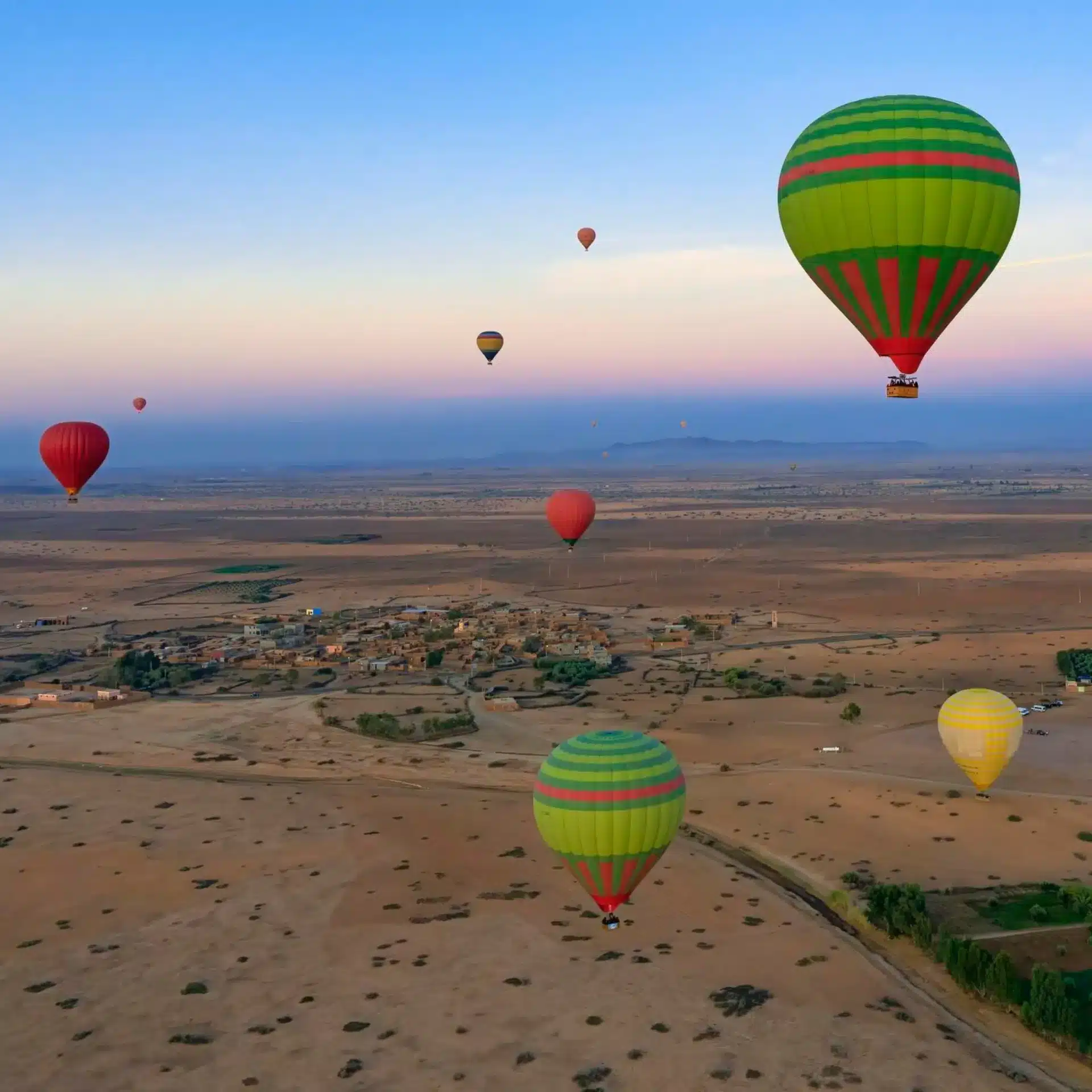 Montgolfières colorées survolant la palmeraie de Marrakech au coucher du soleil